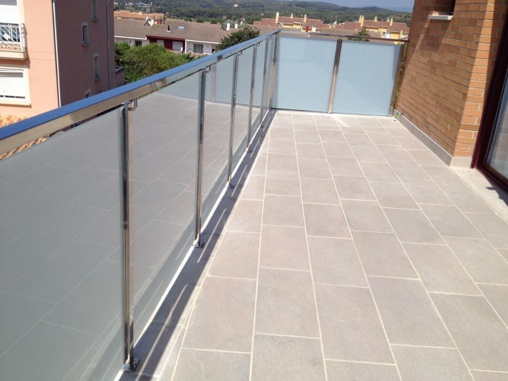 Un balcón con barandilla de acero inoxidable y suelo de baldosas.