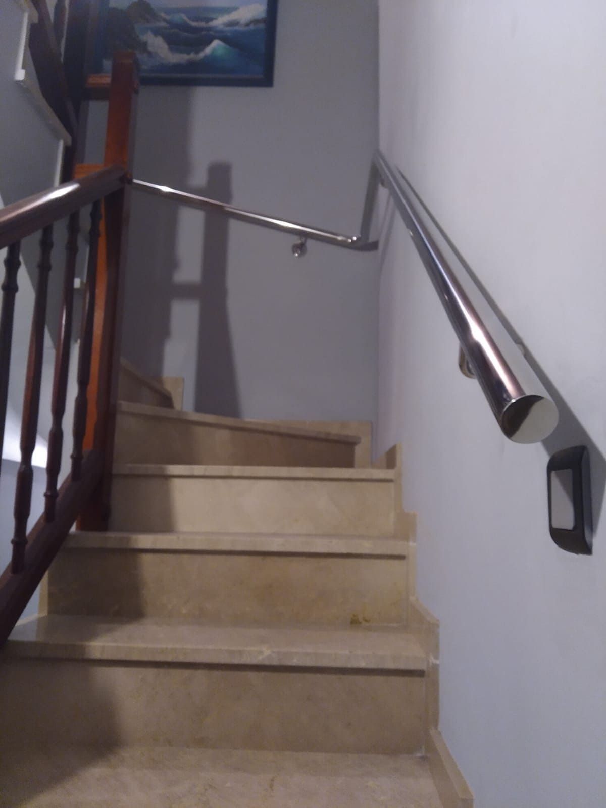 Una escalera con una barandilla de metal y un cuadro en la pared encima.