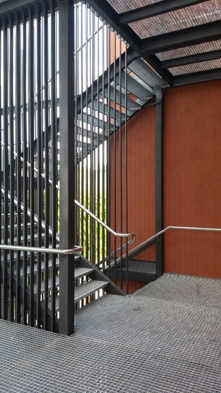 Una escalera con barandilla de metal y una pared roja.
