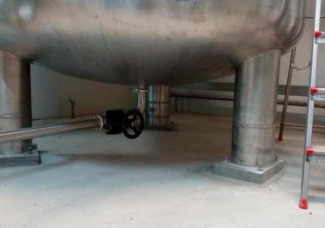 Un gran tanque de acero inoxidable está en una habitación al lado de una escalera.