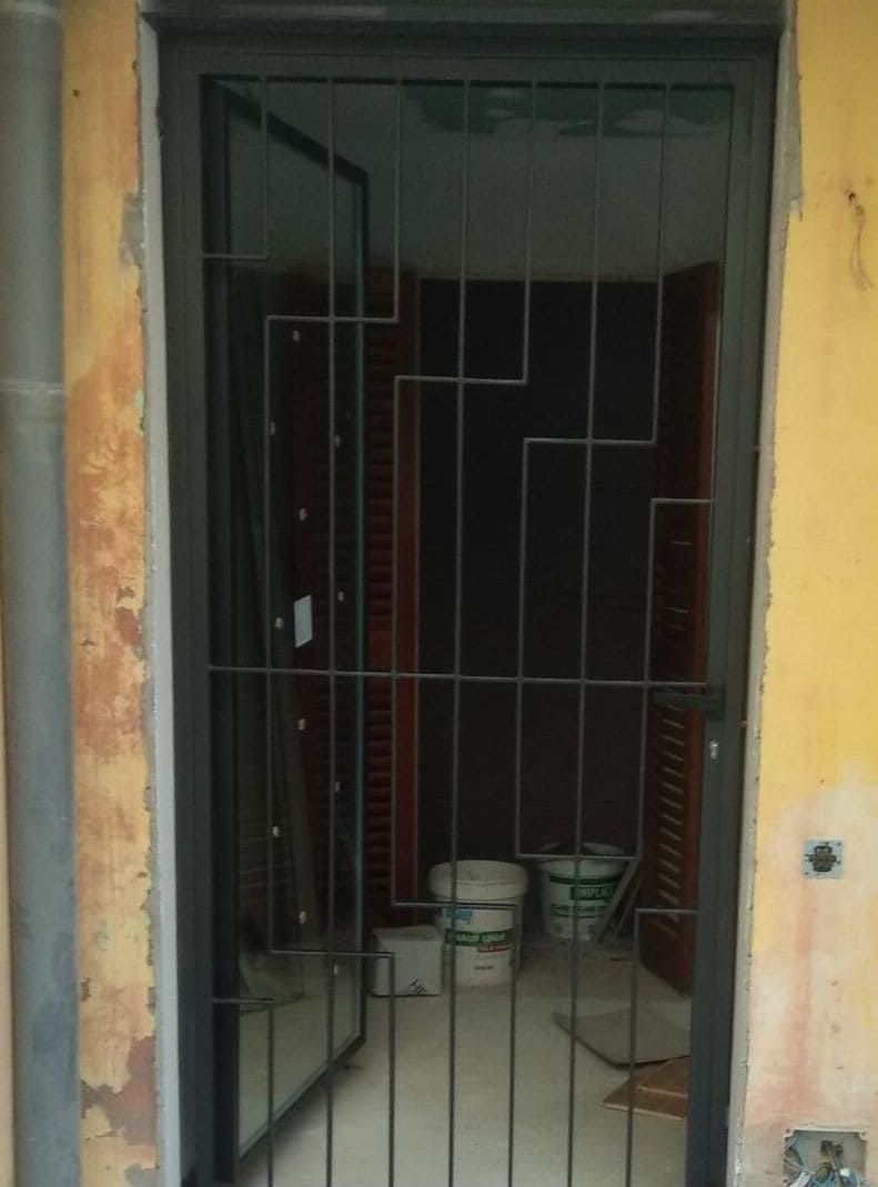 Una puerta con una reja de metal está abierta a una habitación con cubos en el suelo.