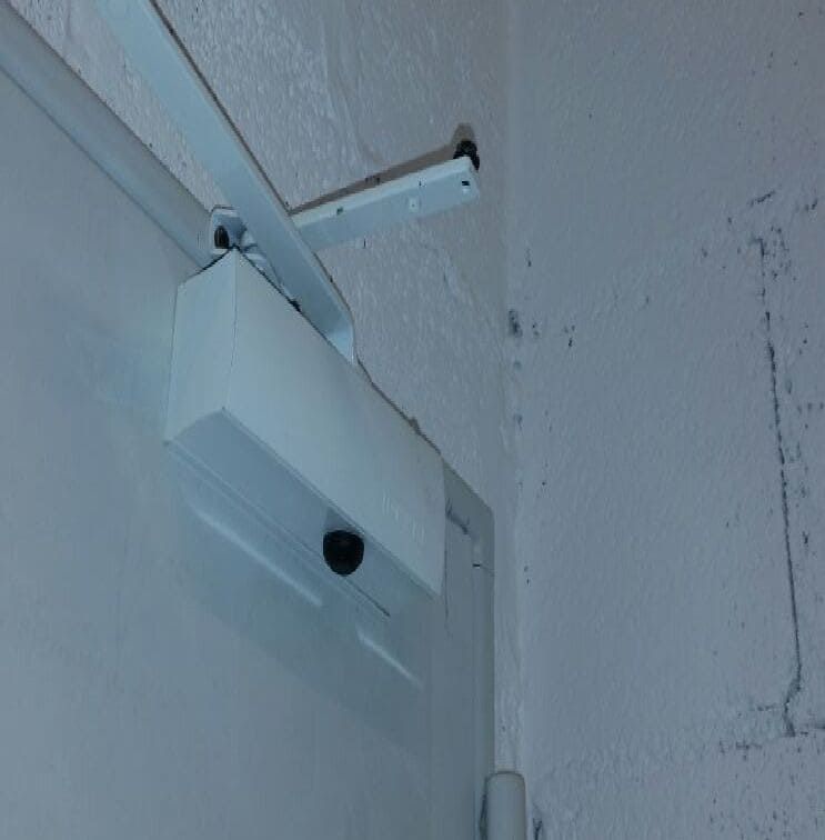 Un cierrapuertas blanco está fijado a una pared blanca.