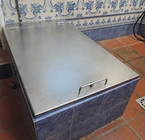 Una caja de acero inoxidable con asa se encuentra sobre un suelo de baldosas.