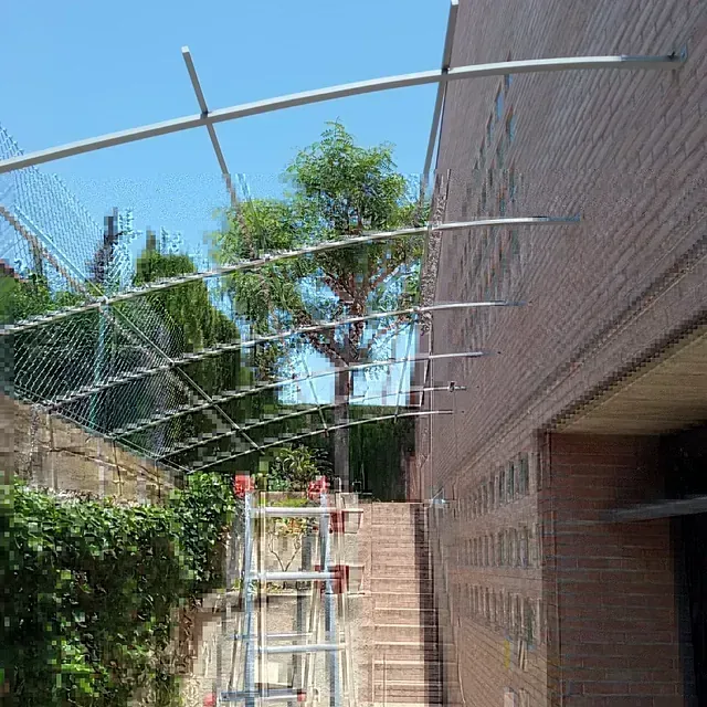 Una escalera está colocada en el costado de un edificio al lado de una cerca de alambre.