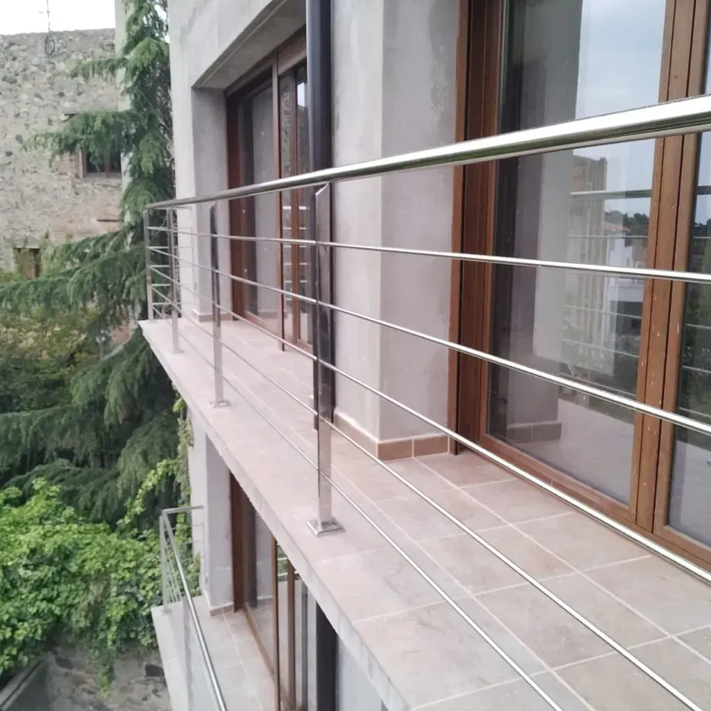 Un balcón con barandilla de acero inoxidable y ventanas de madera.
