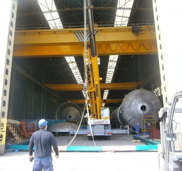 Un gran tanque está siendo levantado por una grúa en un almacén.