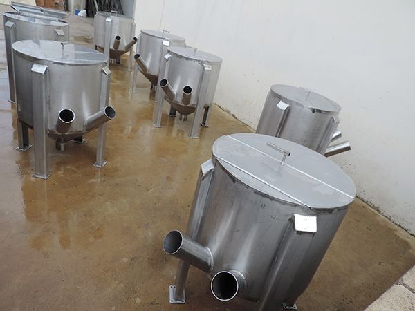 Una fila de tanques de acero inoxidable están alineados sobre un piso de concreto.