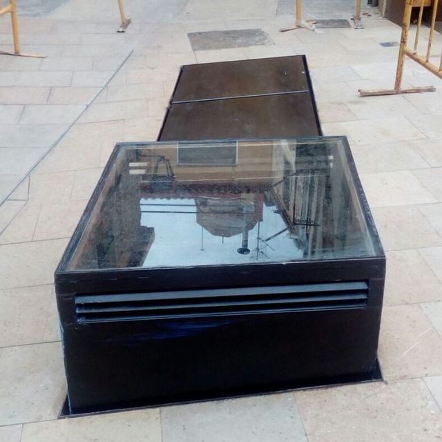 Una caja negra con tapa de cristal reposa sobre un suelo de baldosas.