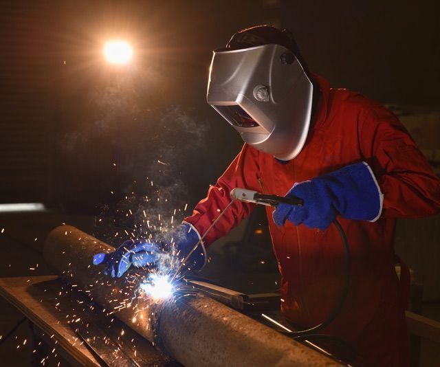 Un hombre que lleva una máscara de soldar está soldando una tubería.