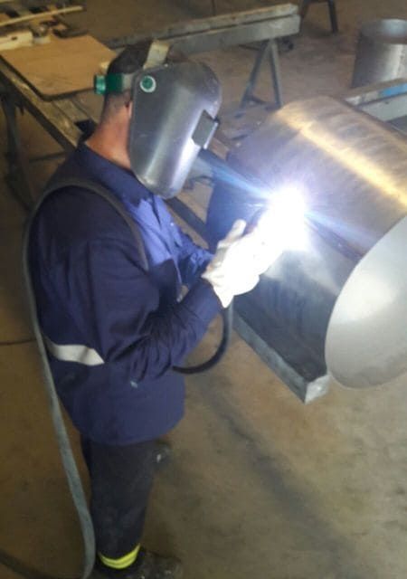 Un hombre que lleva una máscara de soldar está trabajando en una pieza de metal.