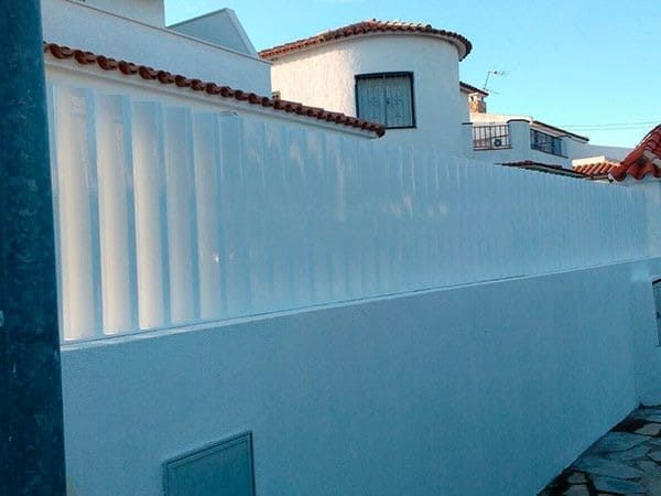 Una valla blanca rodea una casa blanca con techo de tejas rojas.