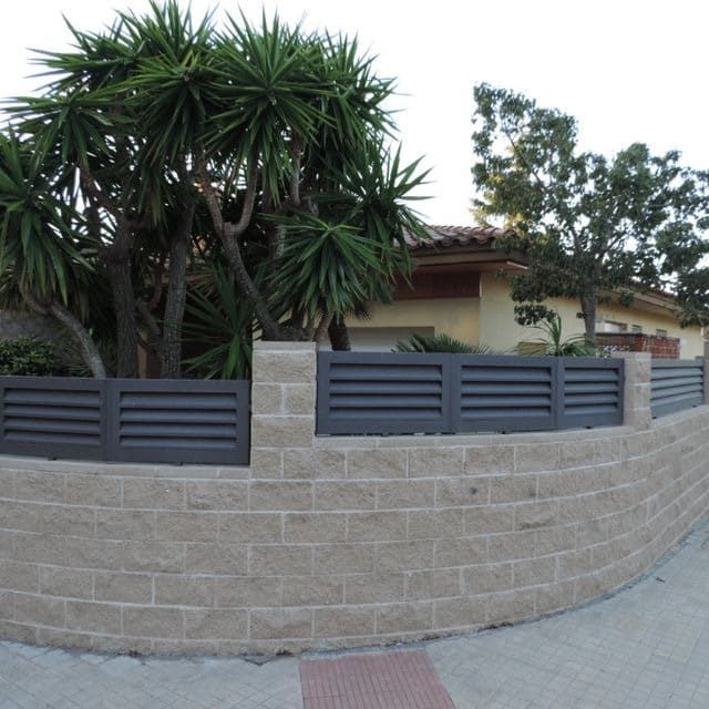 Una pared de ladrillos con una valla negra delante de una casa.