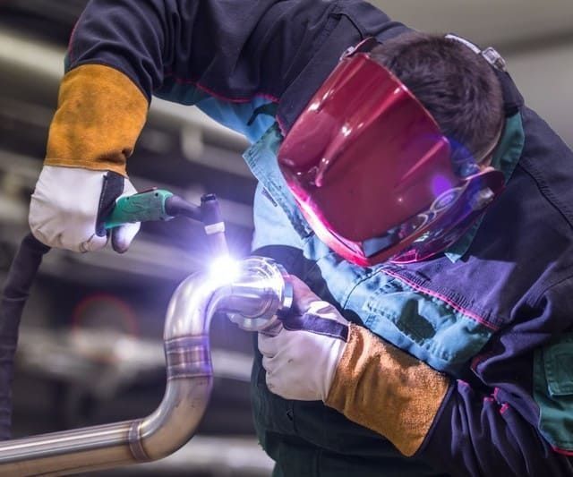 Un hombre que lleva una máscara de soldar está soldando una tubería.