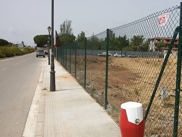 Un bote de basura rojo y blanco se encuentra junto a una cerca de alambre.