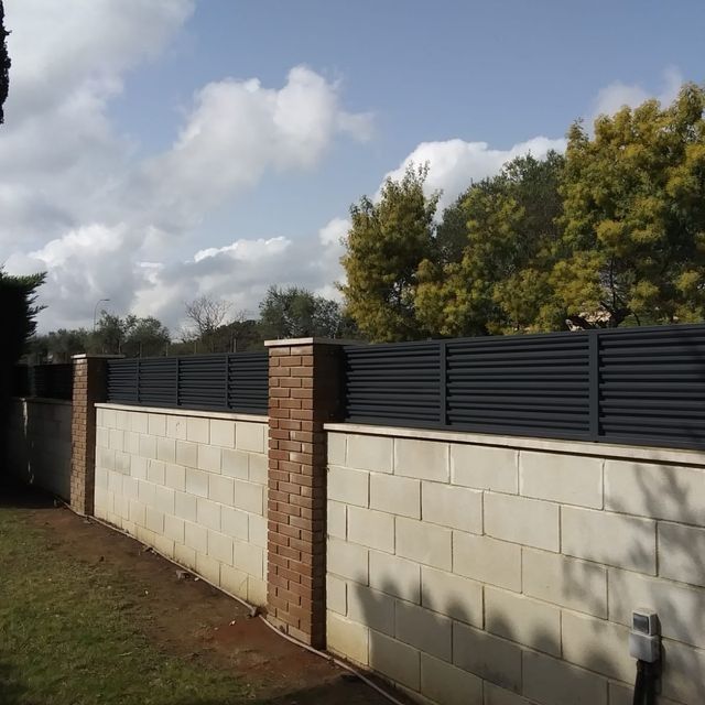 Una pared de ladrillos con una valla negra al fondo.