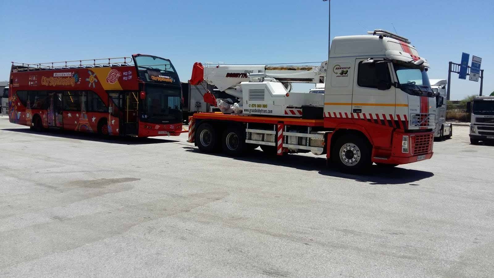 Un autobús rojo está siendo remolcado por un camión blanco
