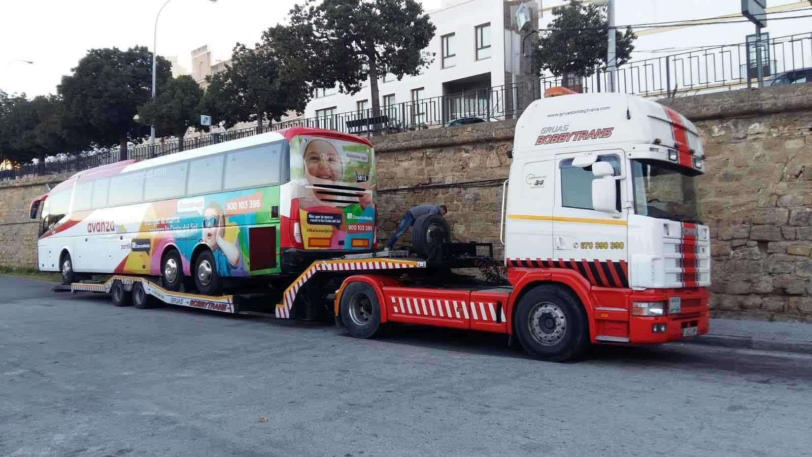 Un autobús colorido está siendo remolcado por un camión semirremolque rojo y blanco.