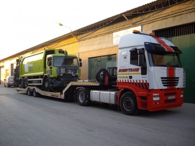 Un camión semirremolque rojo y blanco que transportaba un camión de basura verde.