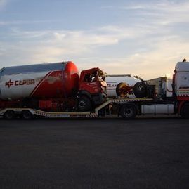Un camión rojo y blanco está siendo remolcado por otro camión.
