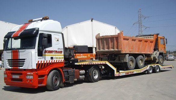 Un camión semirremolque rojo y blanco transporta un camión volquete