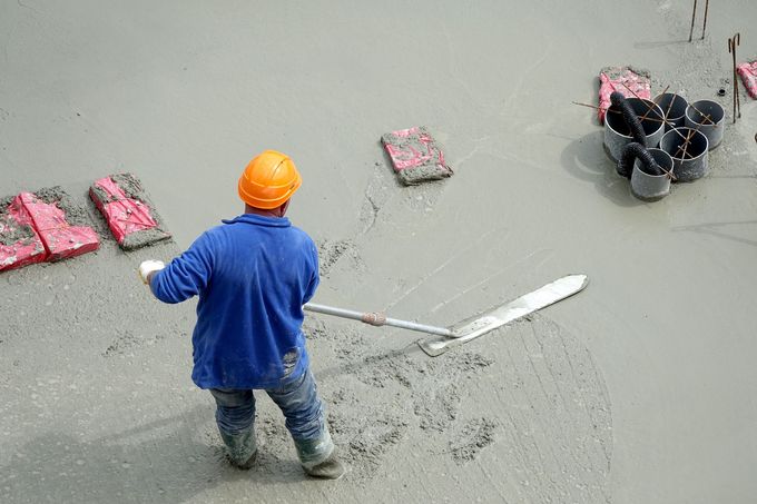 Un ouvrier du bâtiment lisse le béton avec une grande truelle sur un chantier de construction.