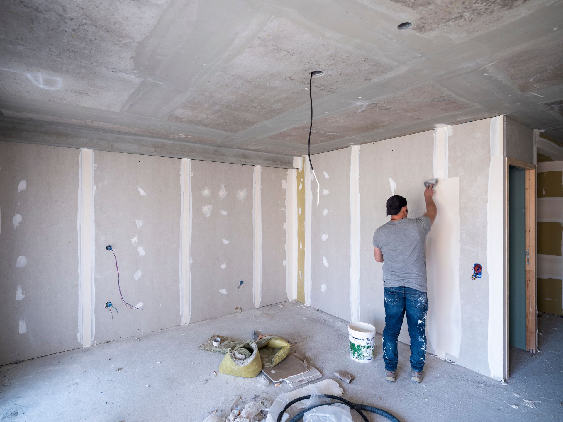 Plaquiste posant des bandes de plâtre sur le mur d'une maison en cours de construction