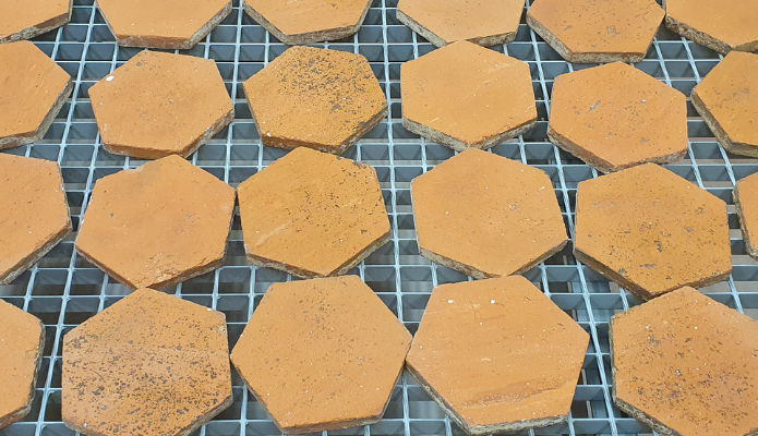 Des rangées de tomettes décapées par aérogommage sèchent sur une grille métallique à l'atelier.