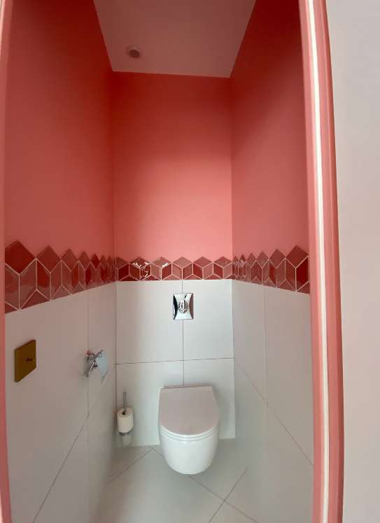 Petite salle de bains rose avec toilettes suspendues et sol carrelé blanc
