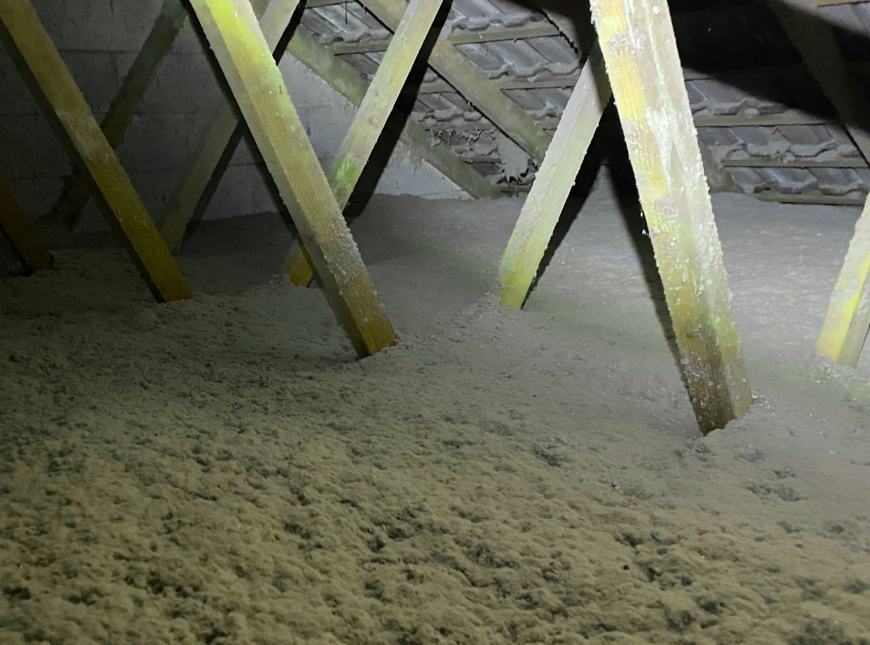 Combles en cours de travaux avec poutres de toit en bois et fragments de laine minérale au sol