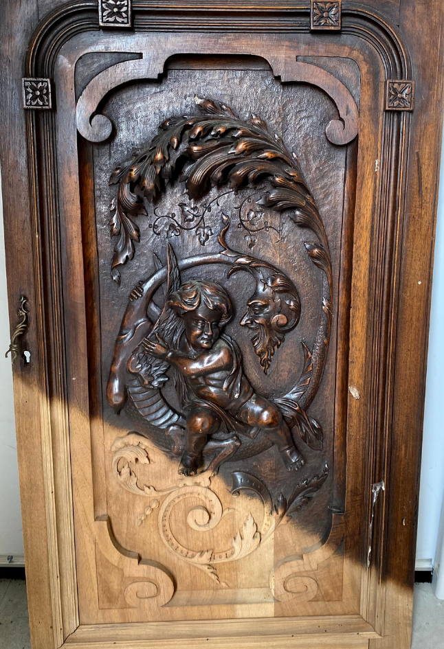 Panneau en bois sculpté orné d'un chérubin et de motifs floraux tourbillonnants sur une porte d'armoire brun foncé