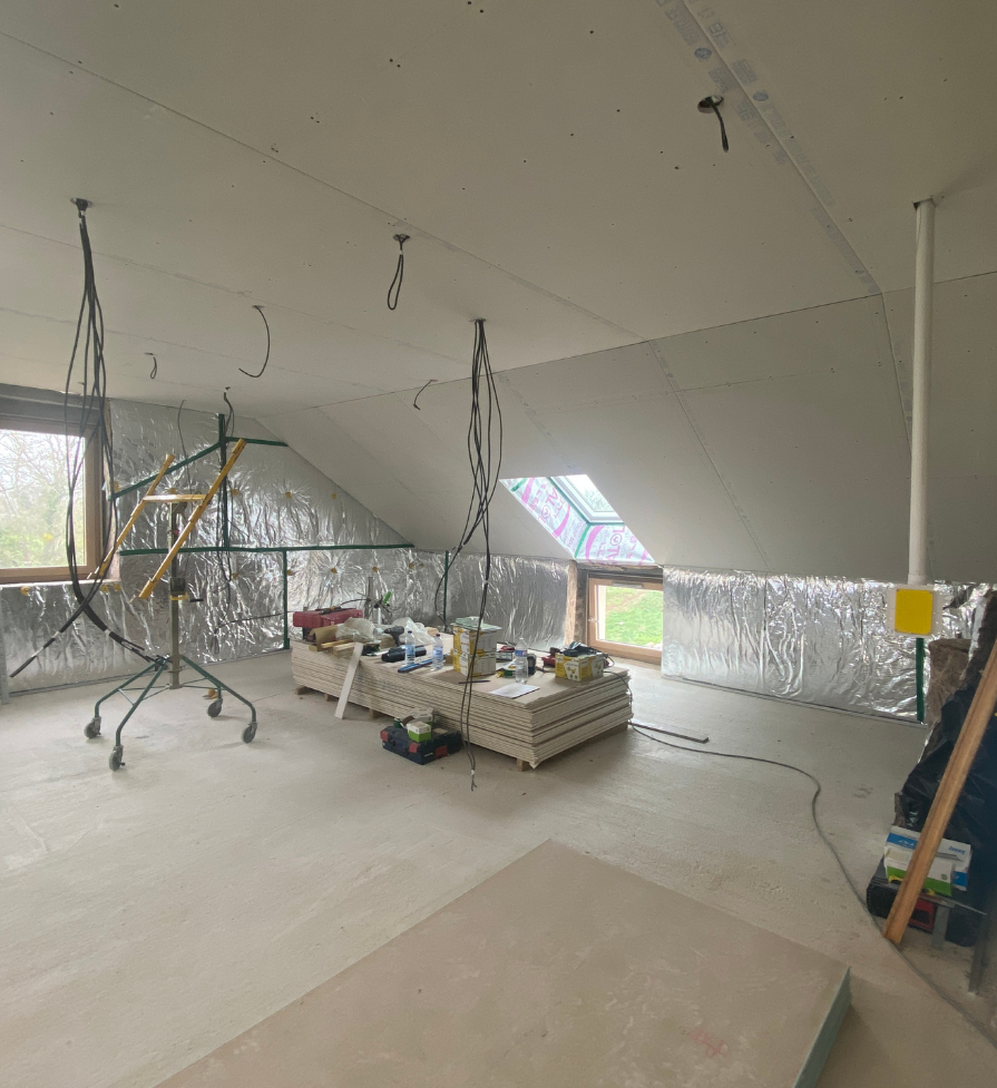 Plafond avec fils électriques apparents, murs recouverts de plastique, fenêtres et matériaux de construction.