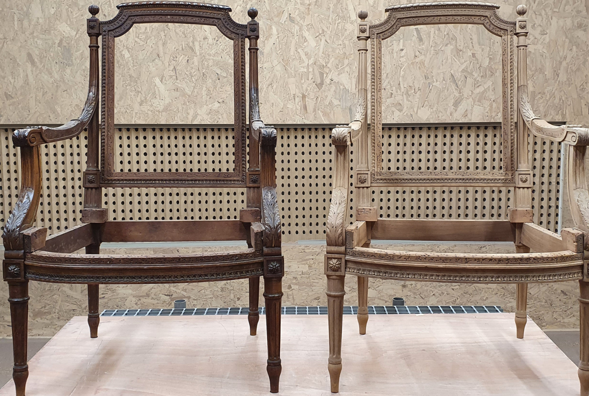 Deux fauteuils en bois finement ouvragés, l'un foncé et l'autre clair, sont disposés côte à côte contre un mur beige.