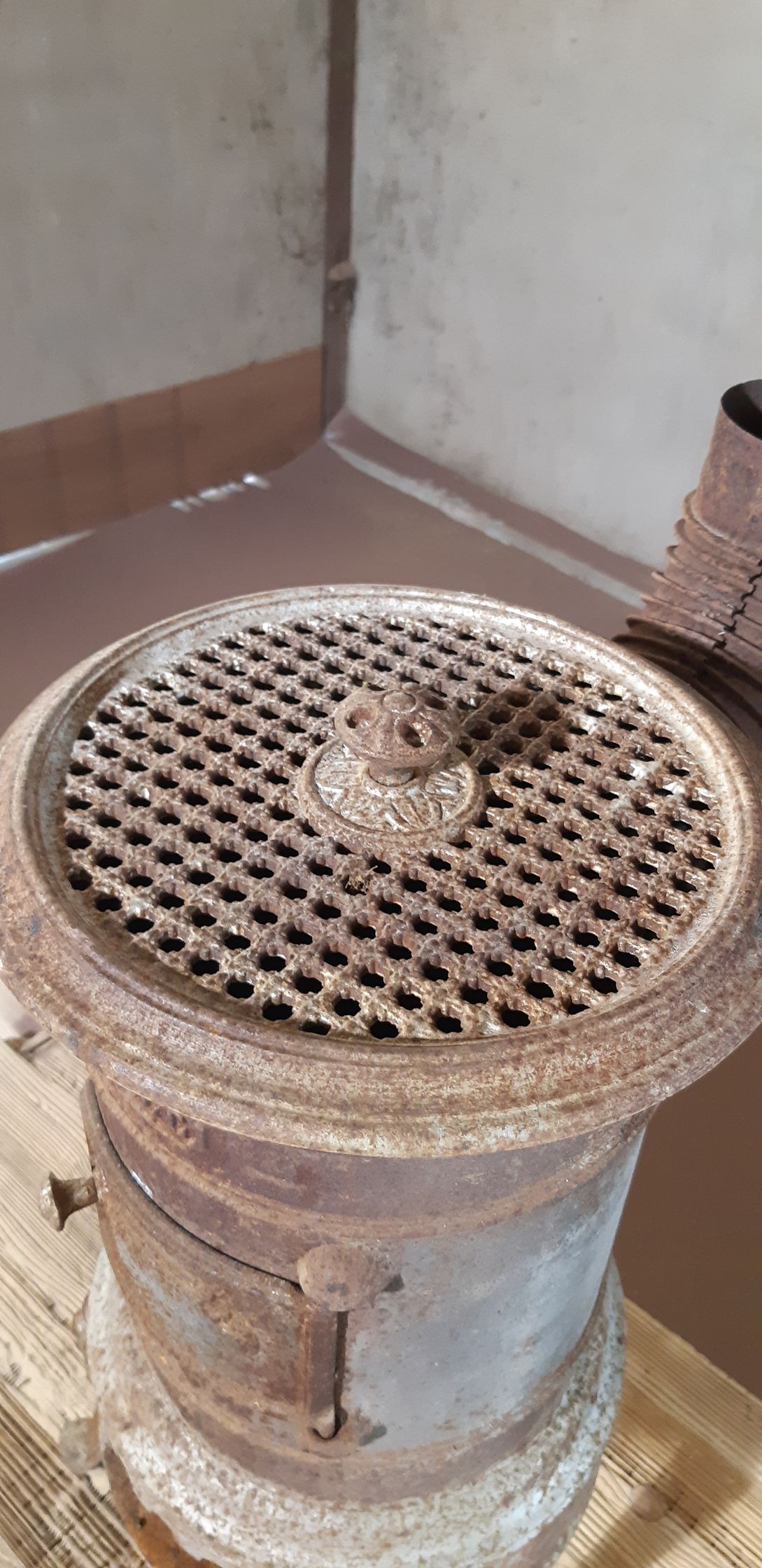 Poêle ou radiateur en métal rouillé avec un dessus perforé, placé contre un mur à l'intérieur.