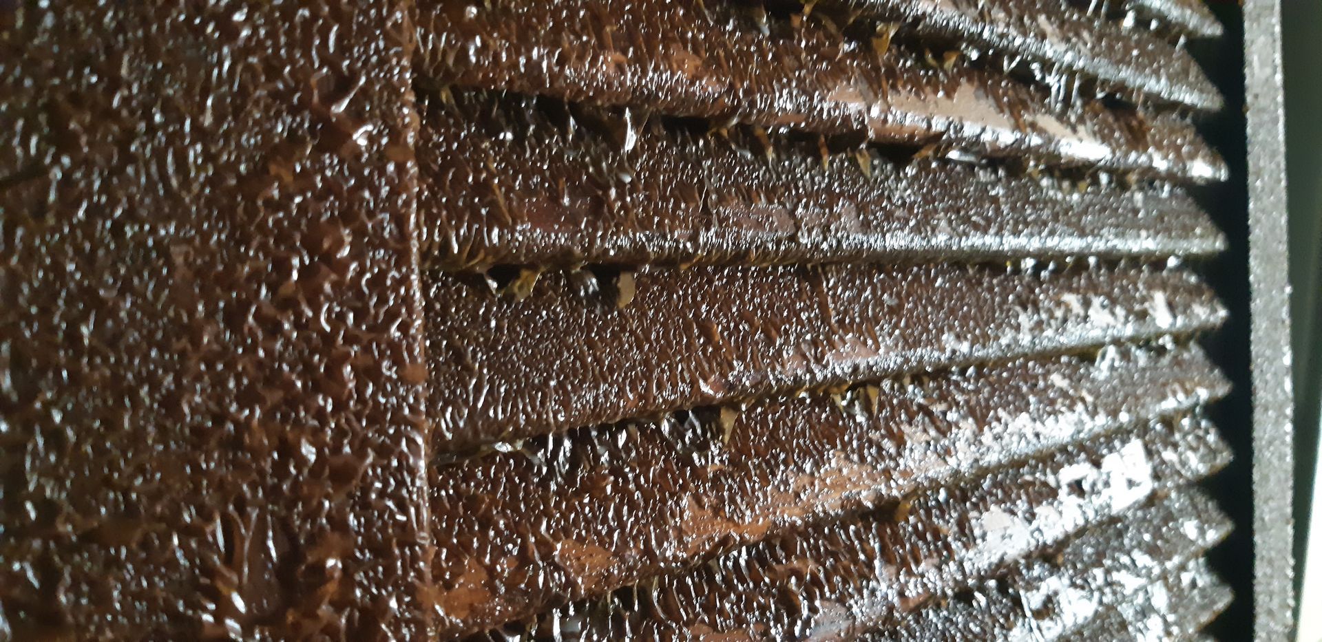 Gros plan sur une surface métallique ondulée, humide et brun rouille, avec des gouttelettes d'eau.