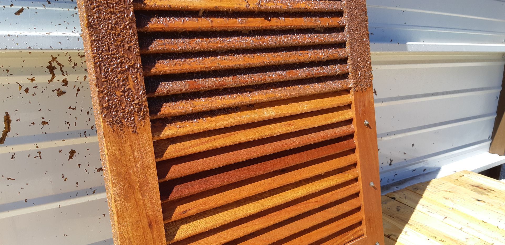 Panneau à persiennes en bois rouillé appuyé contre un bardage gris clair à l'extérieur