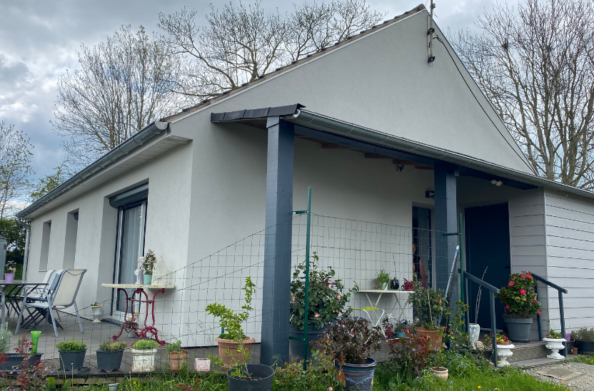 Petite maison blanche aux boiseries bleues et dotée d'un porche couvert, entourée de plantes en pot et d'un jardin.