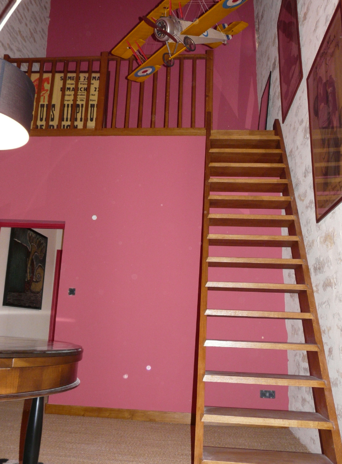 Intérieur rose avec un escalier en bois menant à une mezzanine et un ventilateur de plafond.