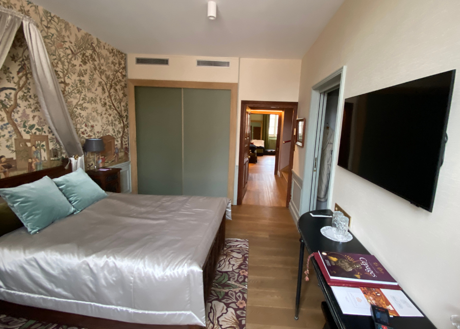 Chambre d'hôtel moderne avec un grand lit, une télévision murale et une vue sur le couloir au-delà de la porte ouverte.
