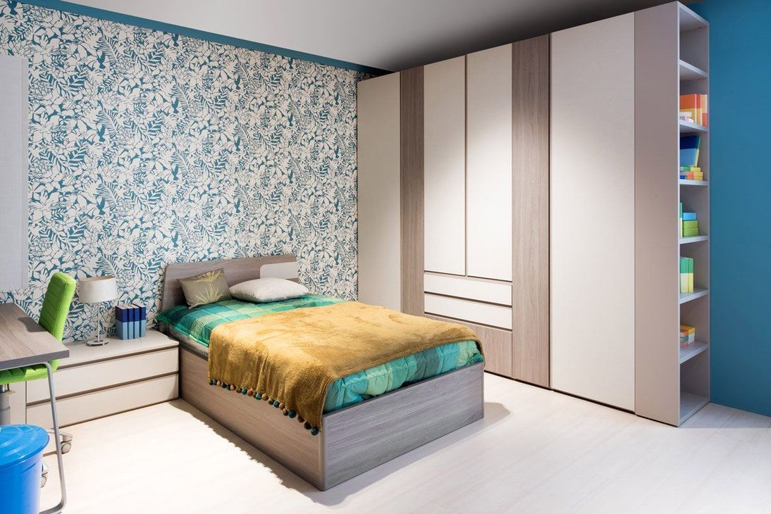 Chambre lumineuse avec papier peint à fleurs, lit bleu, commode blanche et grande armoire.