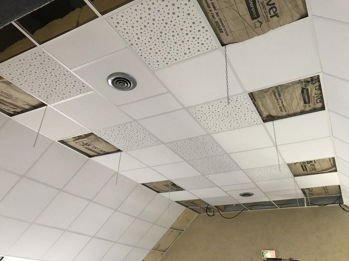 Plafond suspendu avec dalles manquantes et zones exposées dans une pièce de type bureau