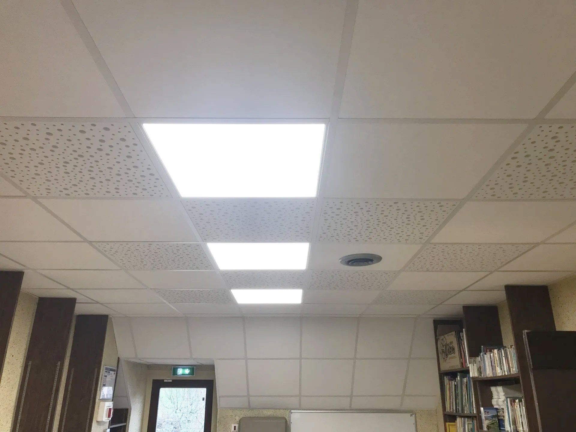 Plafond de bureau avec éclairage fluorescent puissant, dalles acoustiques et étagères latérales.