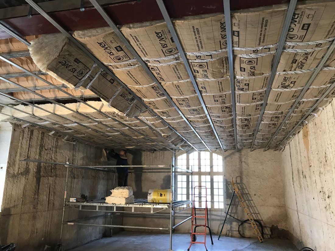 Intérieur d'une pièce en rénovation, avec isolation du plafond apparente, échafaudages et une échelle.