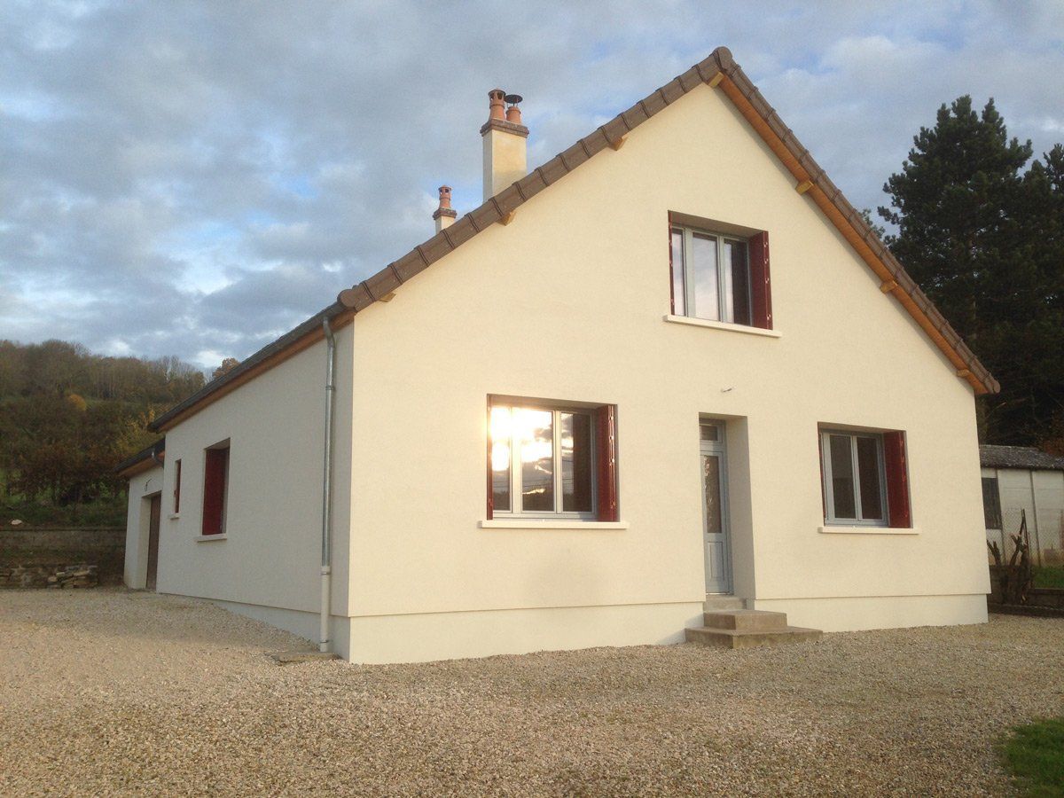 Maison de couleur crème avec un toit rouge et une allée de gravier sous un ciel nuageux