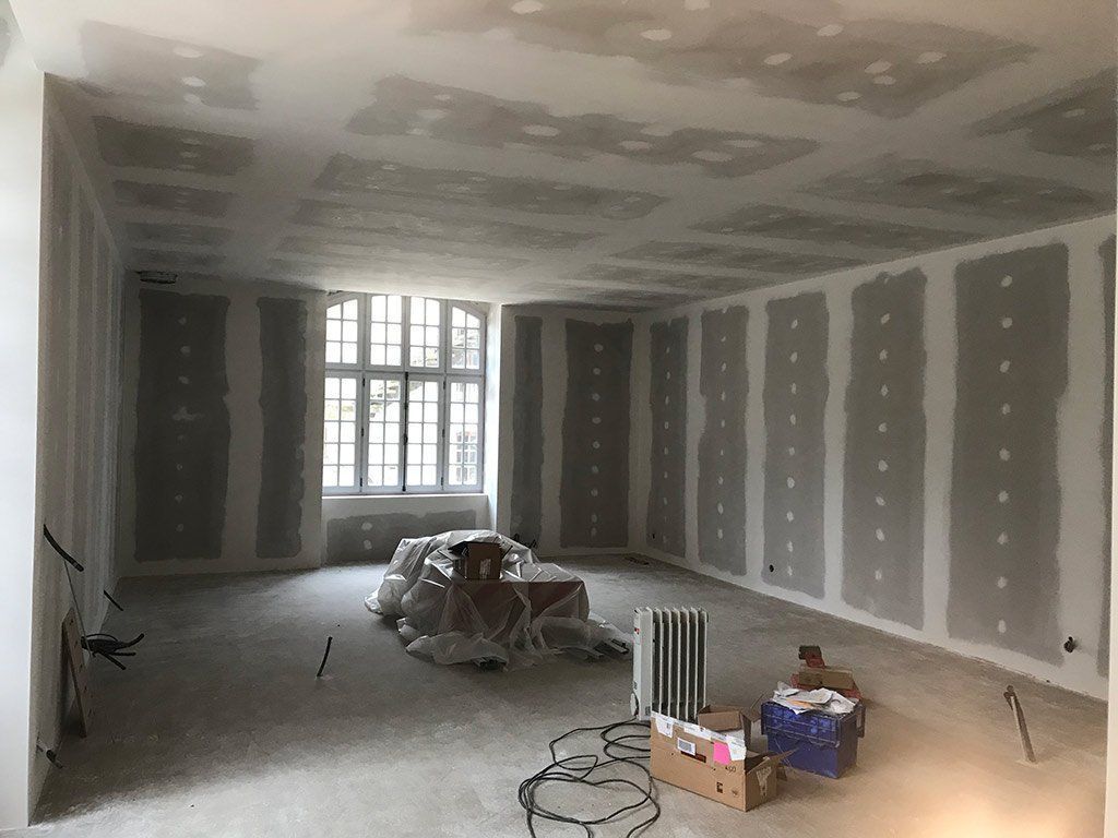 Pièce inachevée avec cloisons sèches, fenêtres et matériaux de construction au sol.