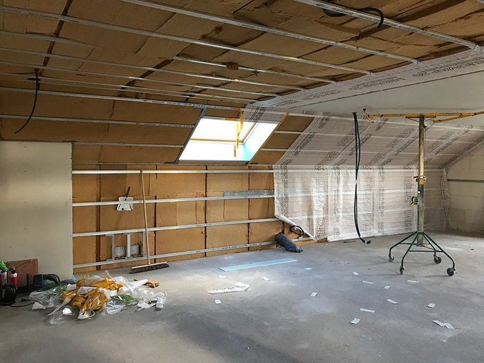 Pièce vide et inachevée avec plafond apparent, puits de lumière, débris au sol et fils électriques pendants.