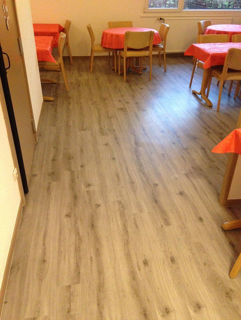 Petite salle à manger avec parquet, nappes rouges, chaises et éclairage chaleureux.