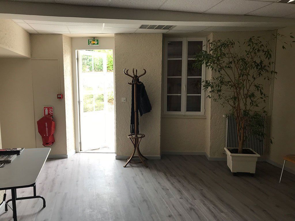 Hall d'entrée vide avec porte blanche, porte-manteau, fenêtre et plante en pot sur sol gris