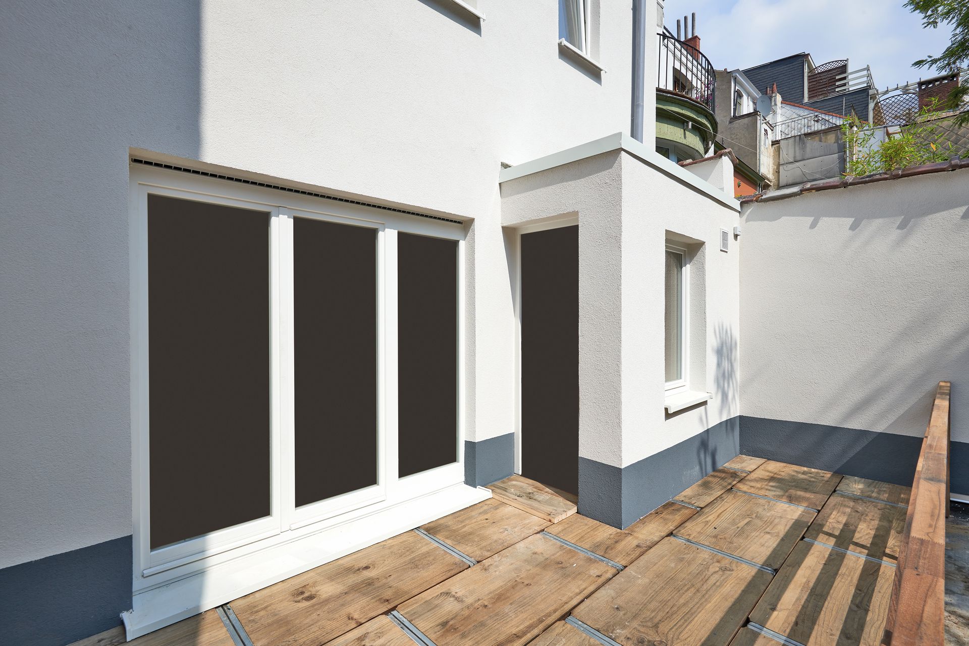 Patio d'une maison moderne avec portes coulissantes en verre, murs blancs et terrasse en bois donnant sur un passage latéral.