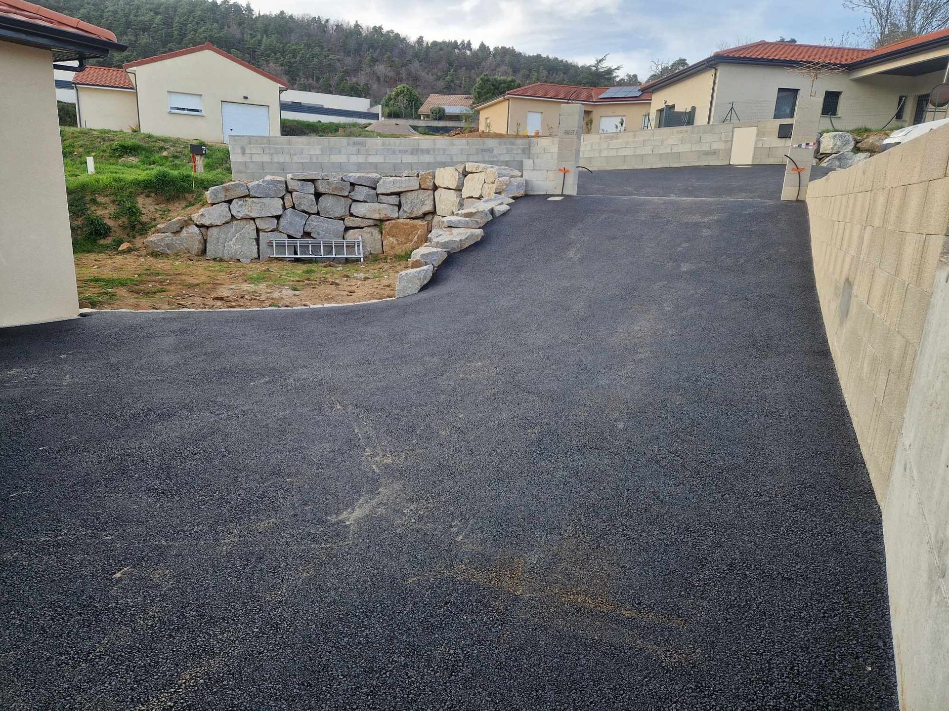Allée asphaltée dans un quartier résidentiel, avec murs de soutènement et maisons en arrière-plan.