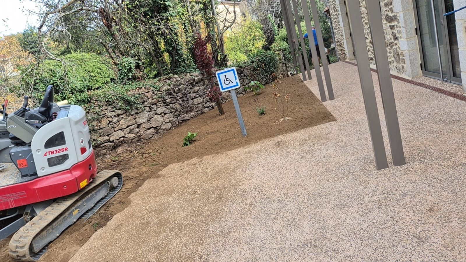 Petite excavatrice à côté d'un chemin de gravier avec panneau d'accessibilité et poteaux.